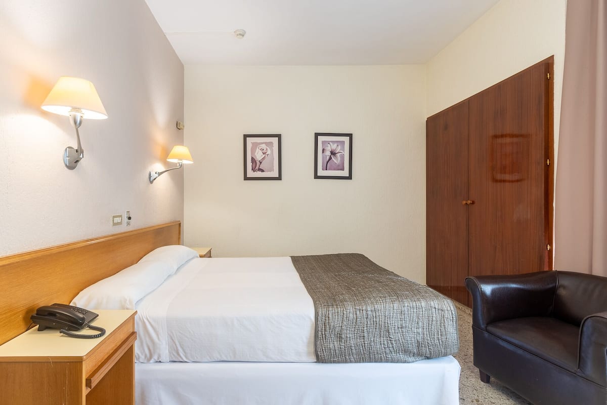 Une chambre d’hôtel comprenant un lit, une table de chevet avec un téléphone, deux lampes fixées au mur et deux tableaux encadrés.