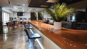 A modern bar area with a long counter, bar stools, and a potted plant. - Hotel Leuka (Alicante)