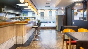 A restaurant interior with a bar area, seating, and a view of the street. - Hotel Leuka (Alicante)