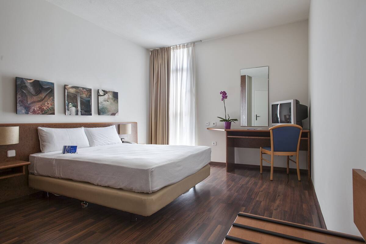 Une chambre d’hôtel avec un lit, un bureau, une chaise, une télévision et trois tableaux accrochés au mur.