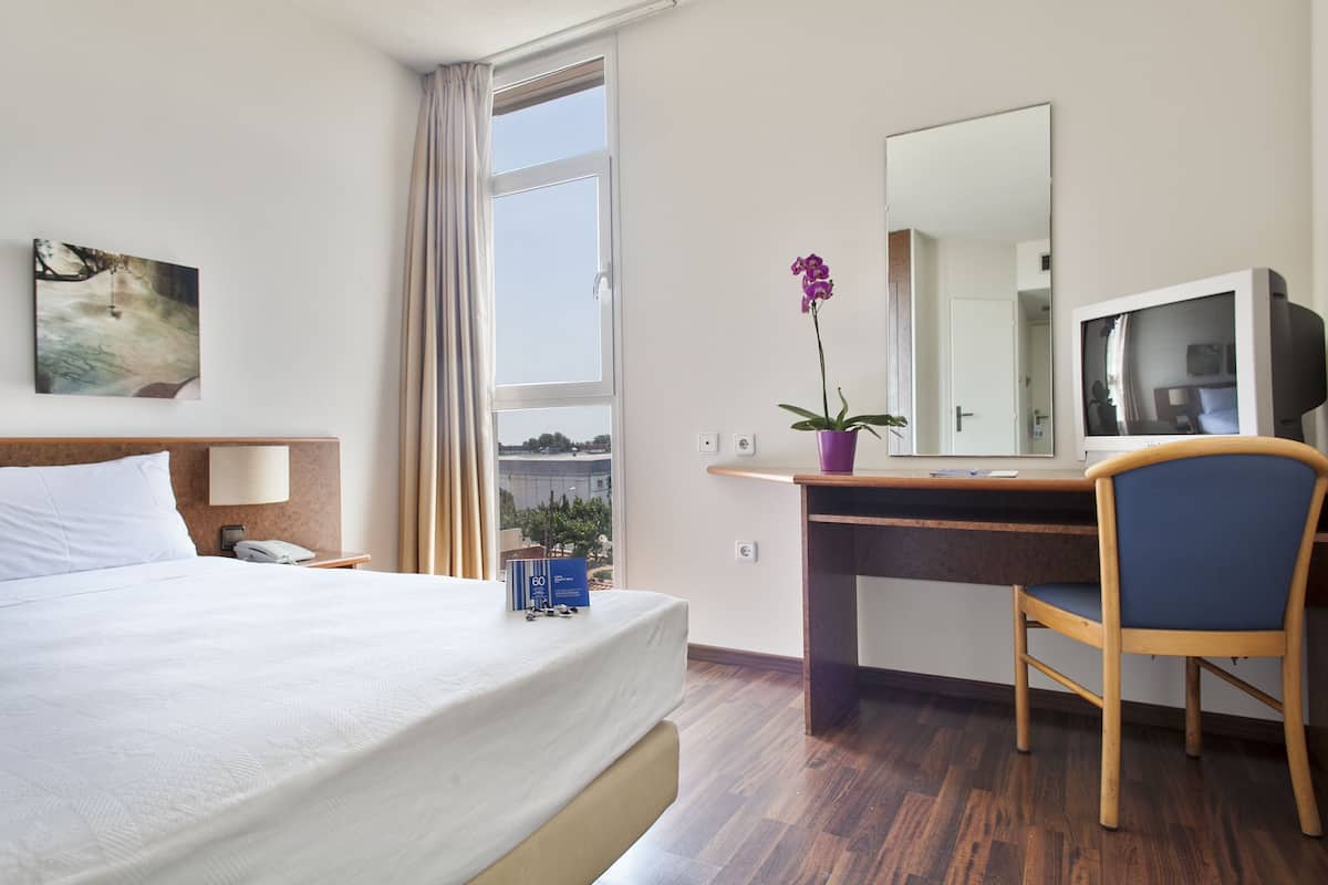 Une chambre d’hôtel équipée d’un lit, d’un bureau, d’une chaise, d’une télévision et d’une fenêtre avec des rideaux.