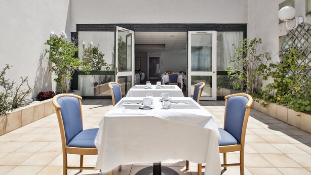 Un espace extérieur aménagé pour les repas, avec des tables et des chaises, une entrée avec une porte vitrée et une vue sur l’intérieur.