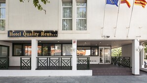 L’entrée d’un hôtel, avec une enseigne indiquant « Hotel Quality Reus », et trois drapeaux flottant sur des mâts.