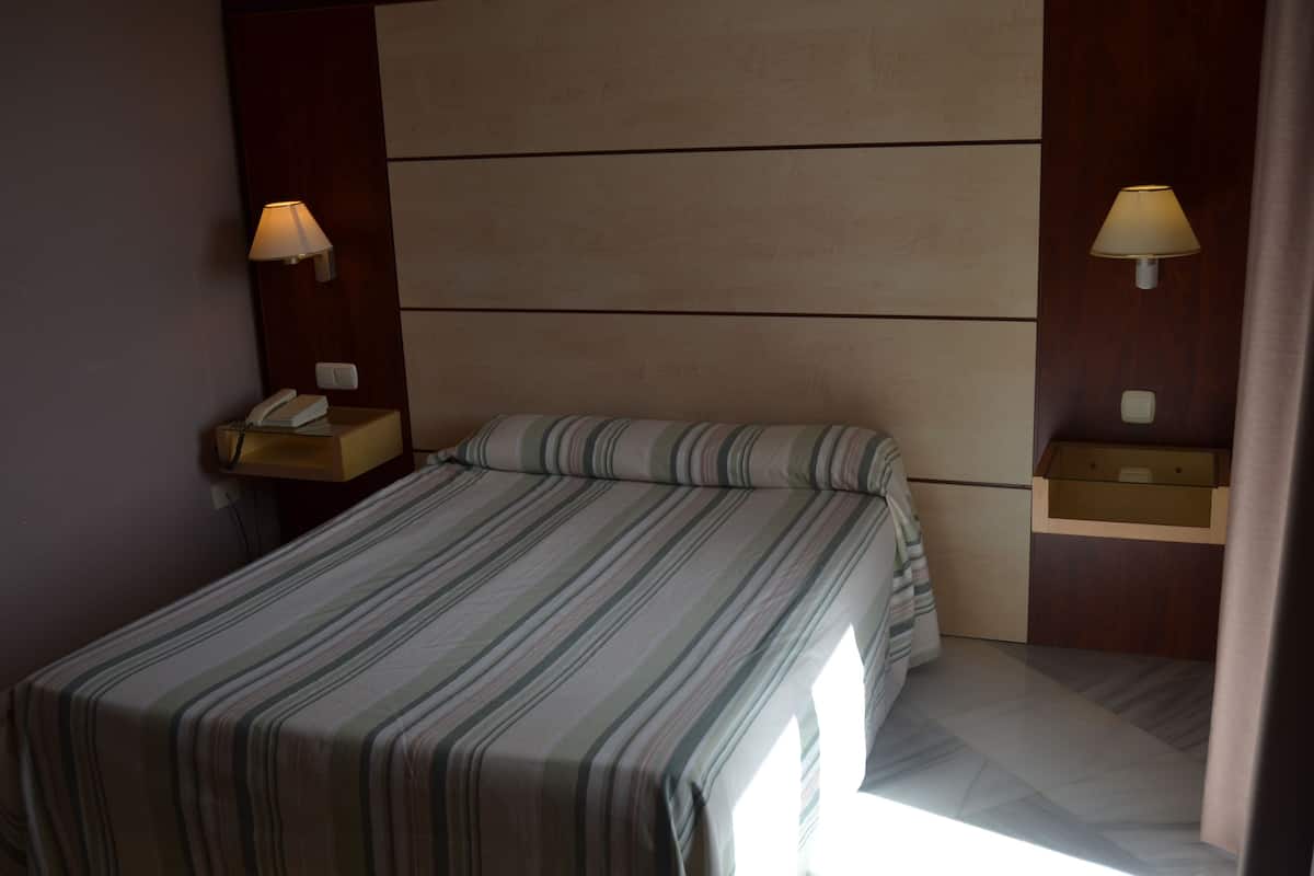 Une chambre d’hôtel avec un lit, deux tables de chevet, une lampe sur chaque table et une petite table de nuit avec un téléphone.