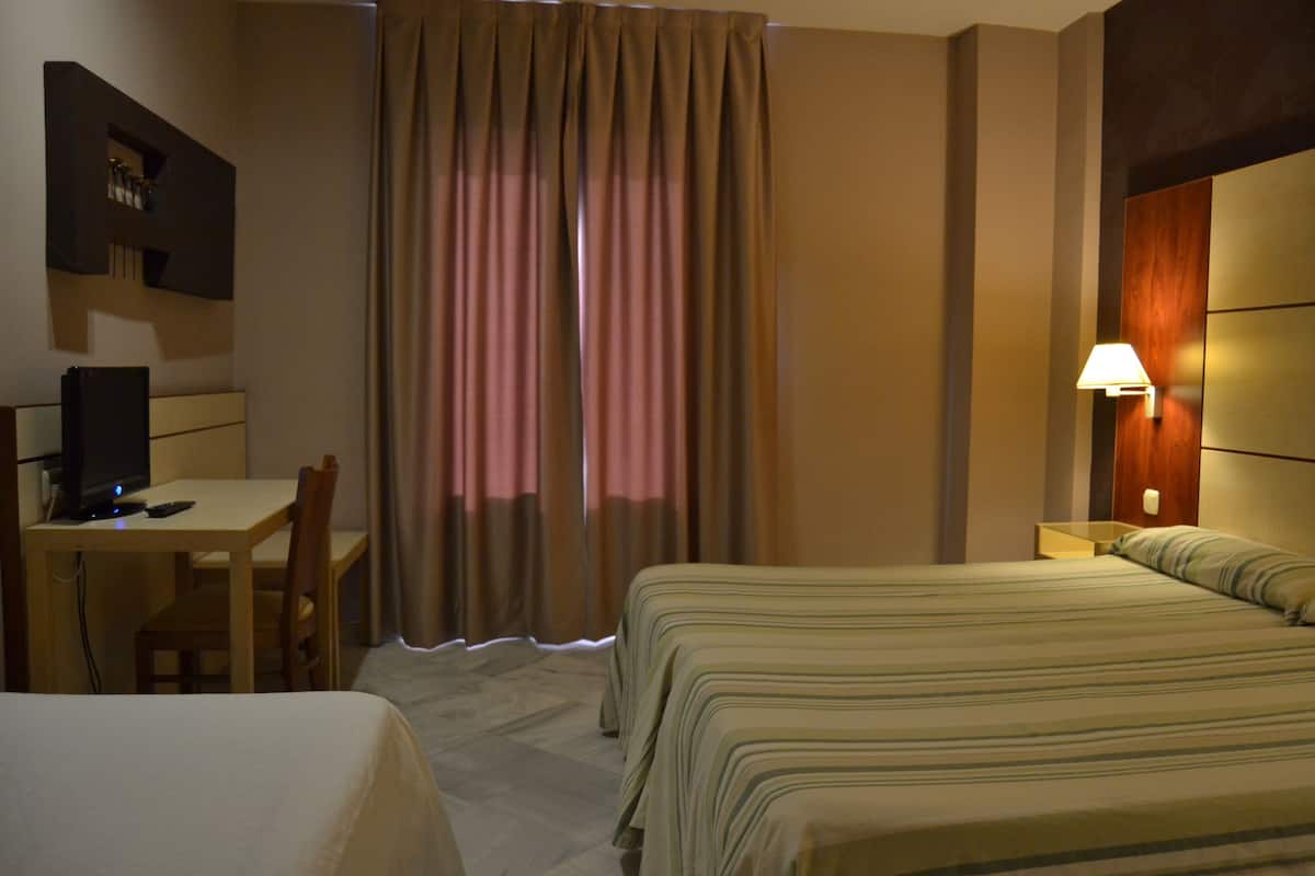 Une chambre d’hôtel avec un lit, un bureau avec une chaise, une lampe et des rideaux.