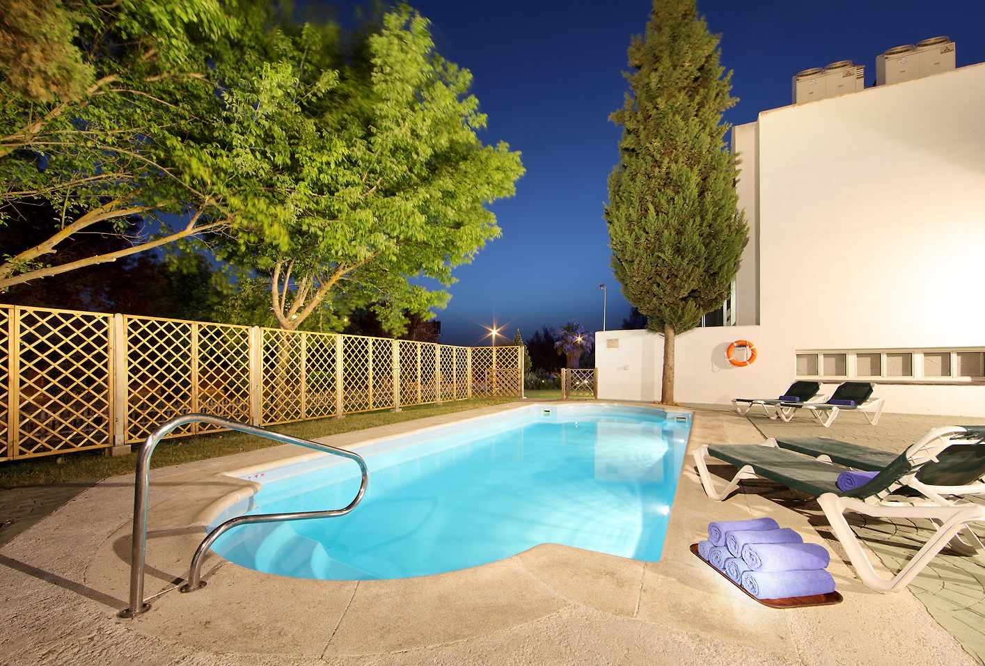 Una piscina amb una escala metàl·lica, gandules i una tanca de fusta.