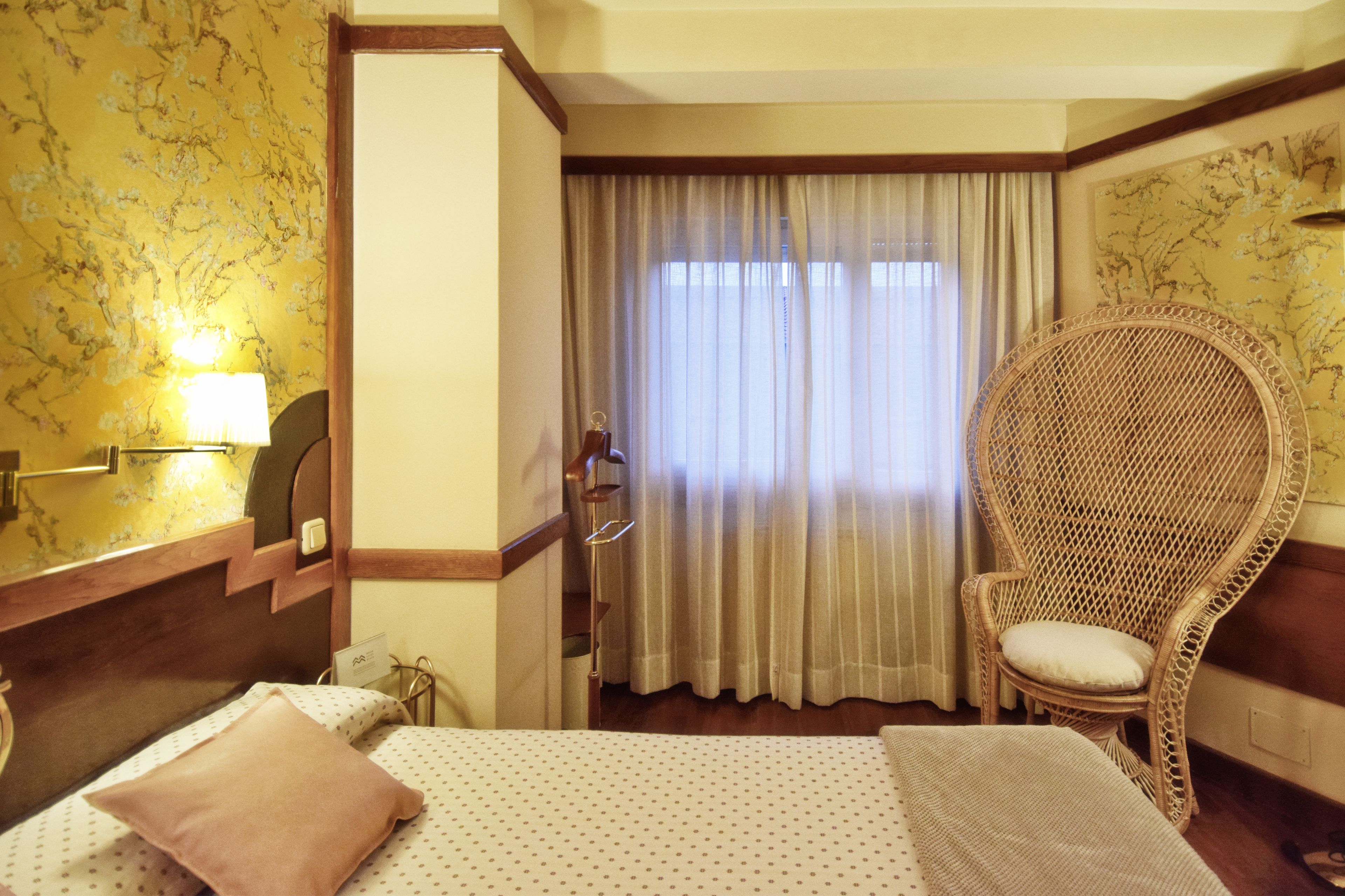A hotel room with a bed, a chair, a lamp, and a window with curtains.
