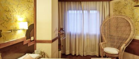 Una habitación de hotel con una cama, una silla, una lámpara y un ventanal con cortinas.