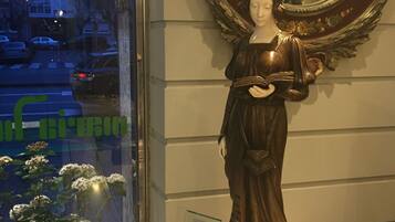 A statue of a woman holding a book, placed on a pedestal with a mirror and floral decorations.