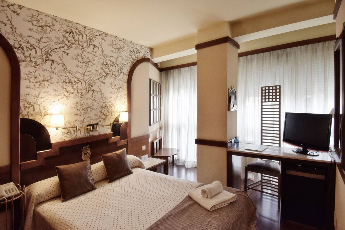 A hotel room with a large bed, a desk with a computer, and a television.
