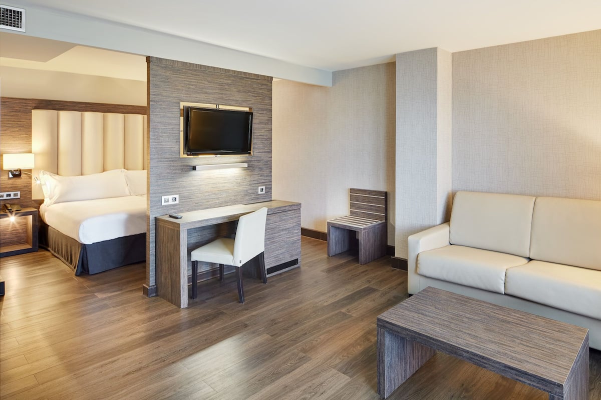 Ein modernes Hotelzimmer mit einem Bett, einem Schreibtisch mit Stuhl, einer Couch und einem an der Wand montierten Fernseher.