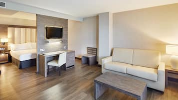 Una habitación de hotel moderna con una cama, un escritorio con una silla, un sofá y un televisor montado en la pared.