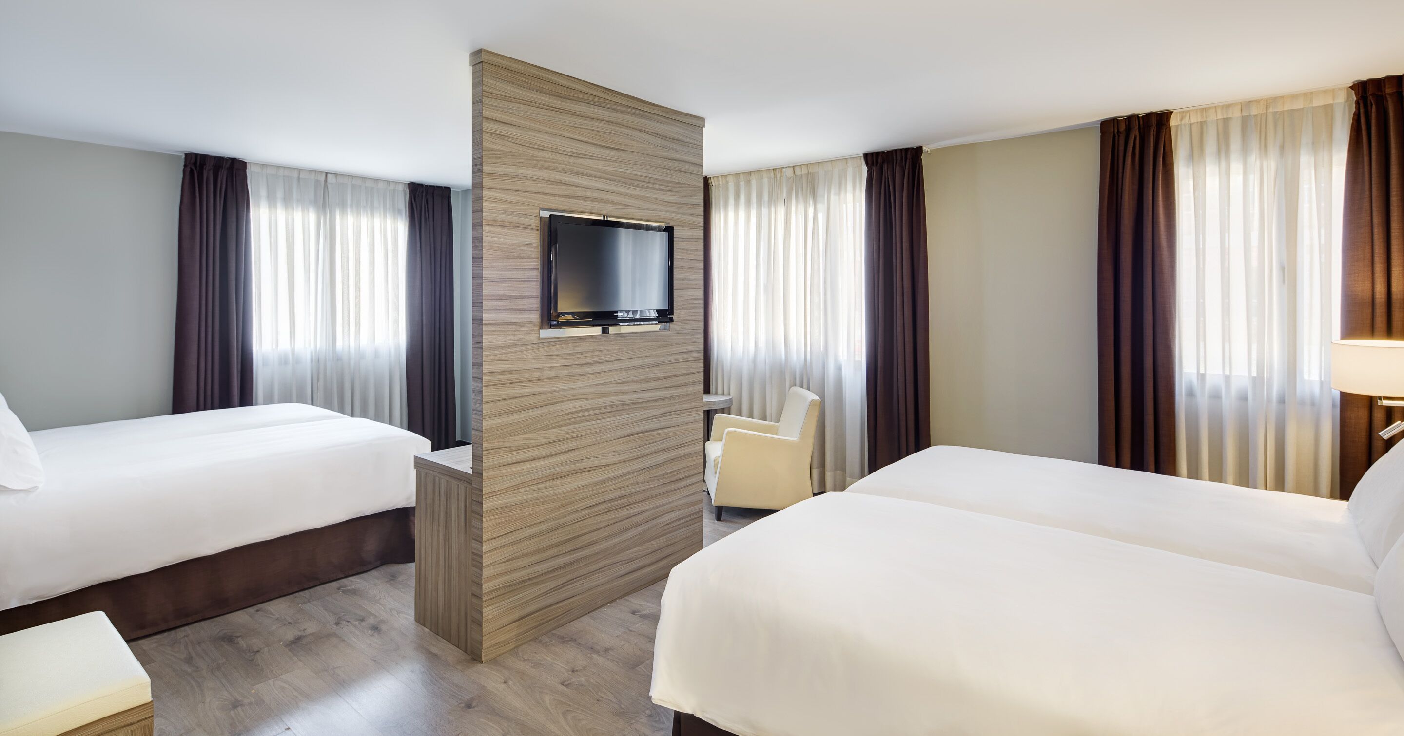 A hotel room with two beds, a TV mounted on a wooden panel, and a chair.