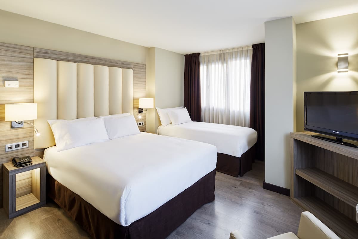 Ein Hotelzimmer mit zwei Betten, einem Fernseher und einem Schreibtisch mit Lampe.