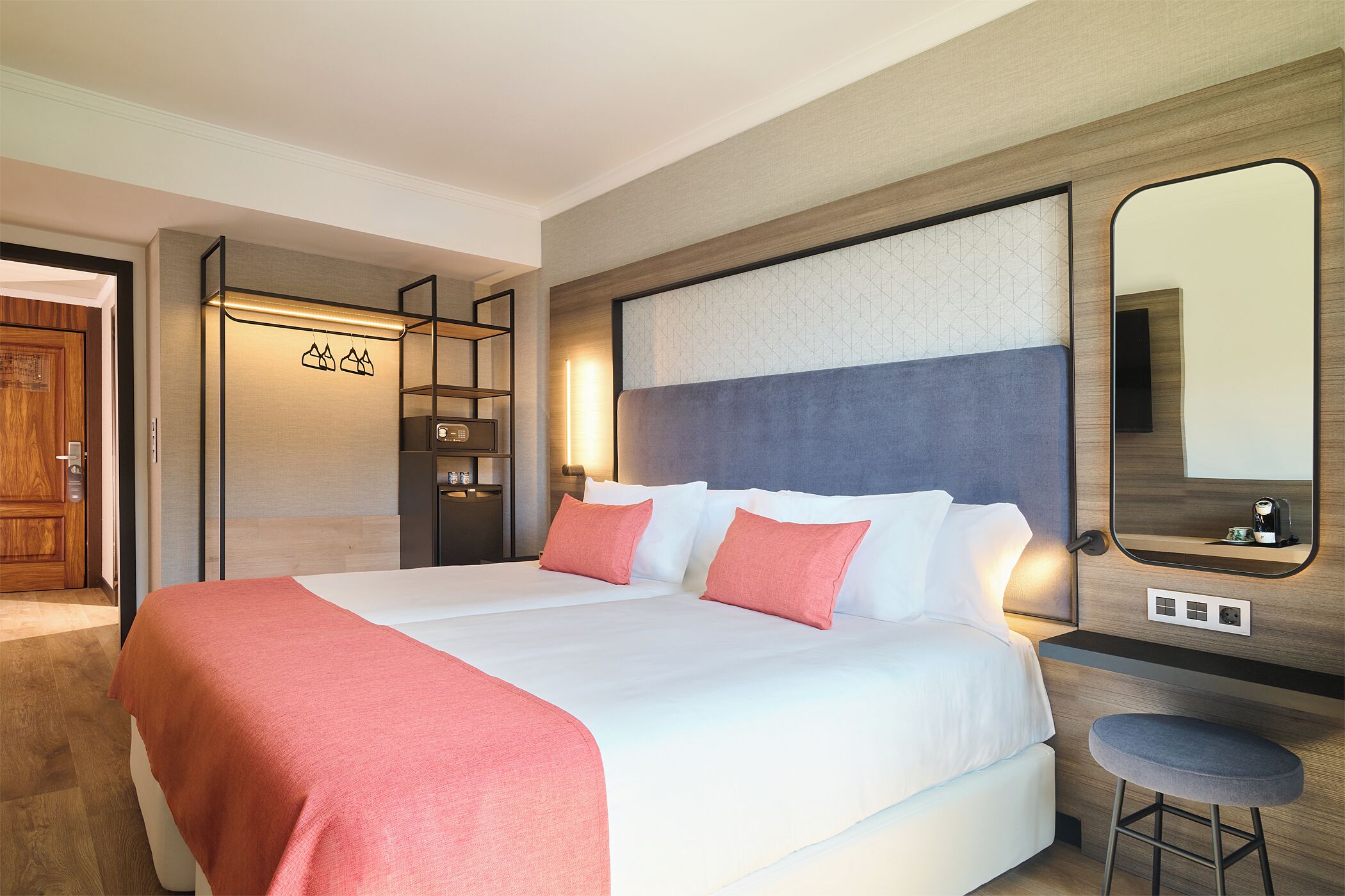 Quarto de hotel moderno com uma cama grande, uma escrivaninha, uma cadeira, um espelho e um guarda-roupa.