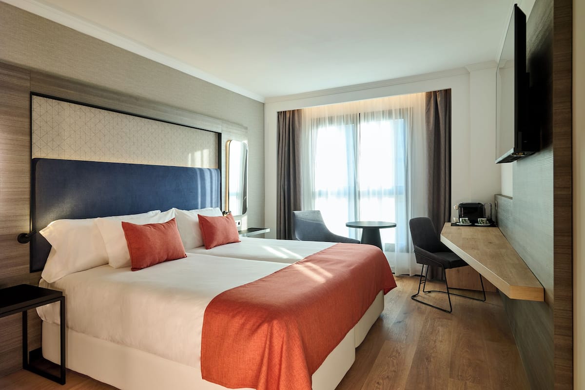 Een hotelkamer met een groot bed, een bureau, een stoel en een aan de muur bevestigde televisie.