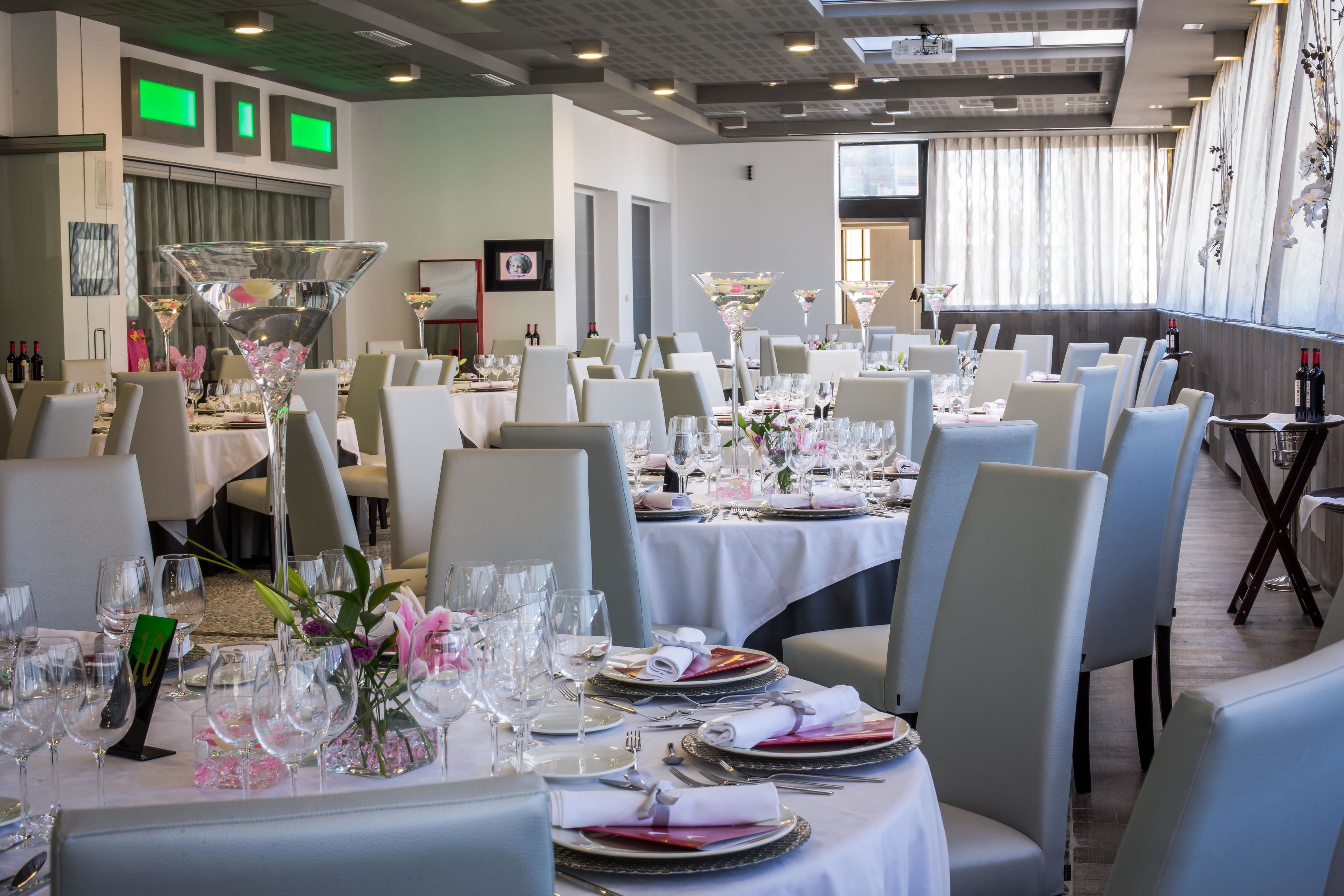 Comedor con mesas redondas dispuestas para una comida formal, con cristalería transparente y centros de mesa florales.