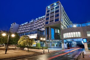 Un edificio de hotel con la señalización "Gran Hotel Luna de Granada", un área de estacionamiento público y una entrada bien iluminada.