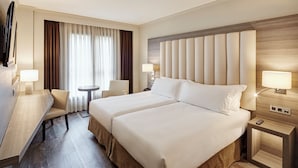 Une chambre d’hôtel avec un grand lit, deux tables de chevet, un bureau avec une chaise, une petite table ronde et un téléviseur.