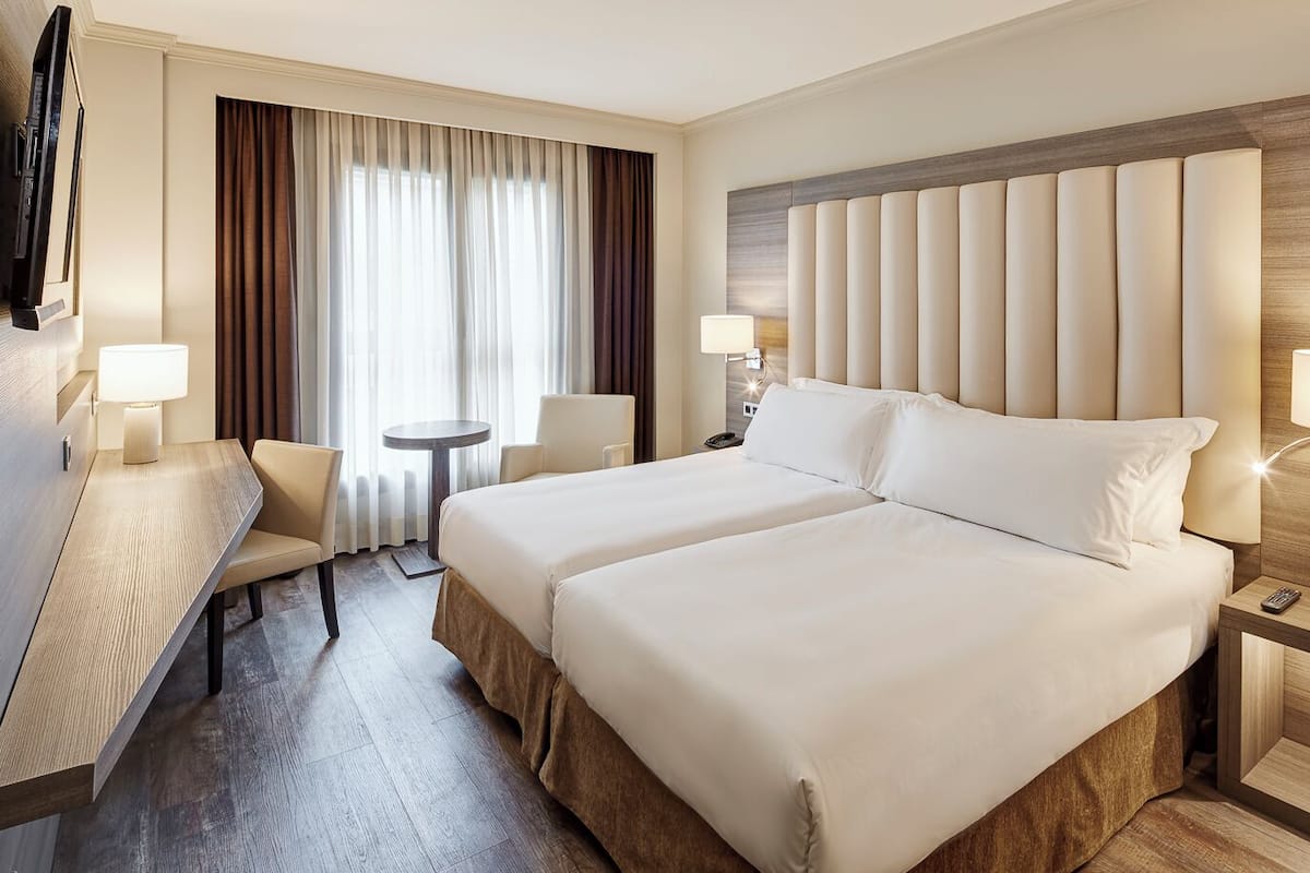 Ein Hotelzimmer mit einem großen Bett, zwei Nachttischen, einem Schreibtisch mit Stuhl, einem kleinen runden Tisch und einem Fernseher.