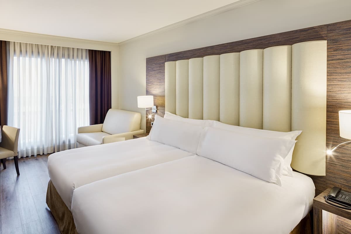 Ein Hotelzimmer mit einem großen Bett, einem Schreibtisch mit Stuhl, einem Fernseher und einem Fenster mit Vorhängen.