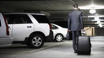 Un hombre con traje camina con una maleta en un estacionamiento.