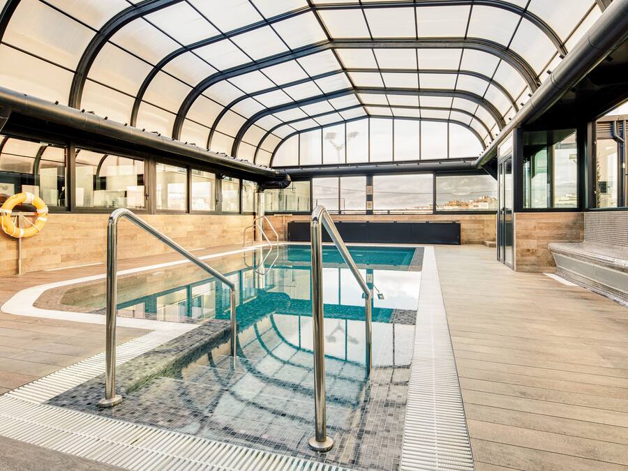 An indoor swimming pool with glass walls, a lifebuoy, and a wooden deck.