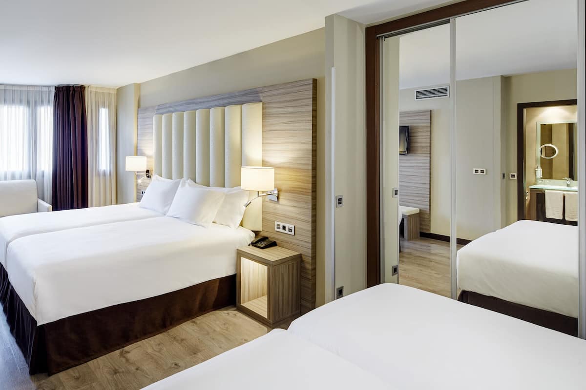 Ein Hotelzimmer mit zwei Betten, einer Sitzecke mit einem Sessel, einem kleinen Tisch und einem Spiegel.