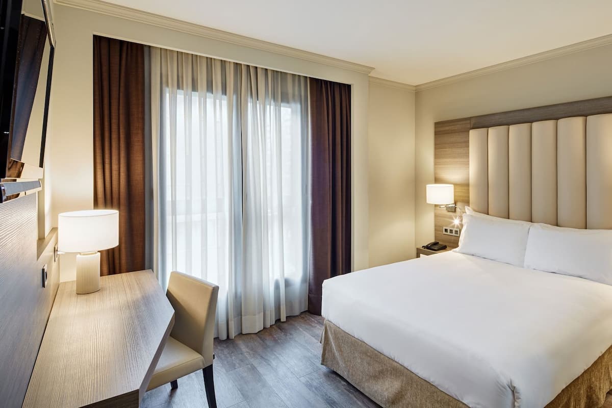 Een hotelkamer met een groot bed, een bureau, een stoel en een raam met gordijnen.
