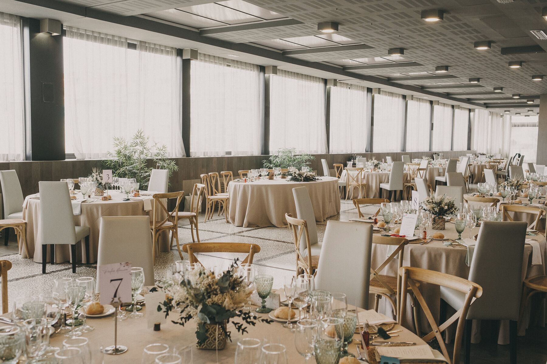 Un salón de banquetes con mesas redondas, sillas y centros de mesa florales.