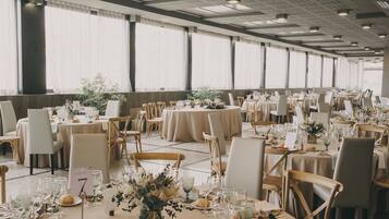 Un salón de banquetes con mesas redondas, sillas y centros de mesa florales.