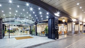 Entrada de hotel con fachada de vidrio, mostrador de recepción y cartel con texto en varios idiomas.