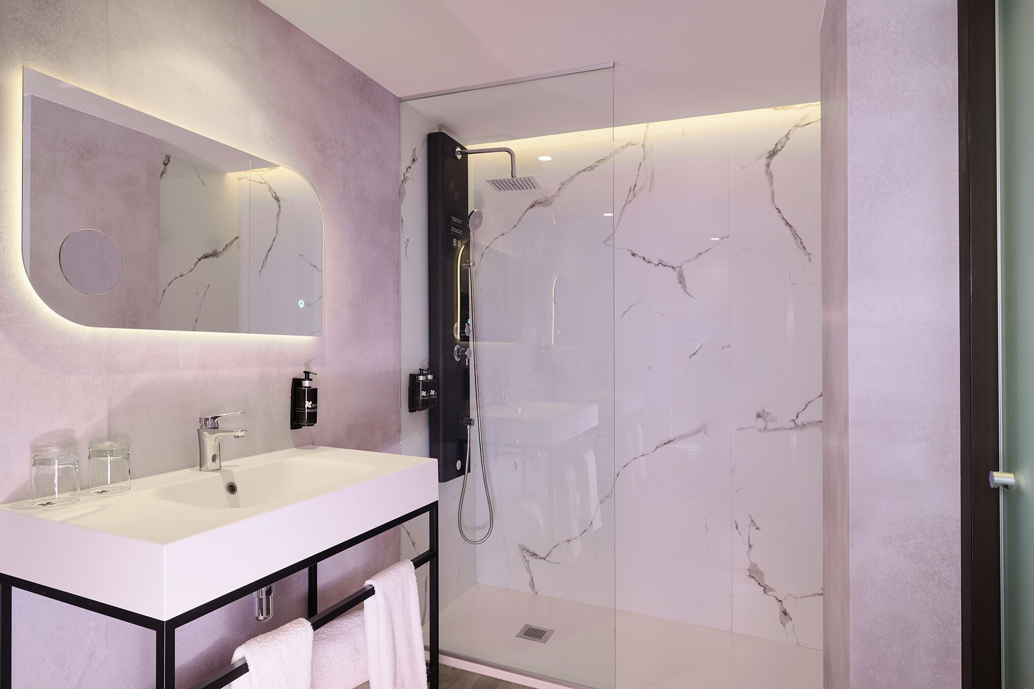 A modern bathroom with a large mirror, a white sink, and a glass-enclosed shower.