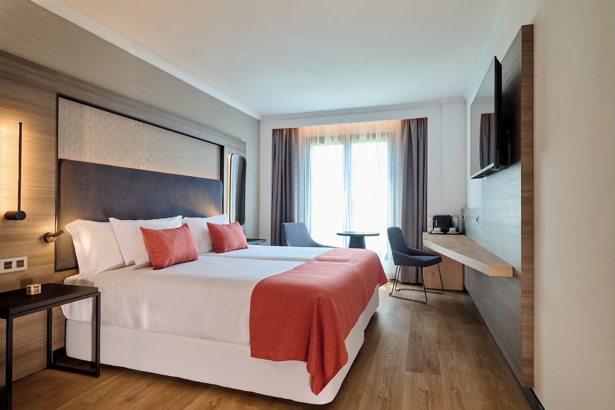 Een hotelkamer met een groot bed, een bureau, een stoel, een televisie en een raam met gordijnen.