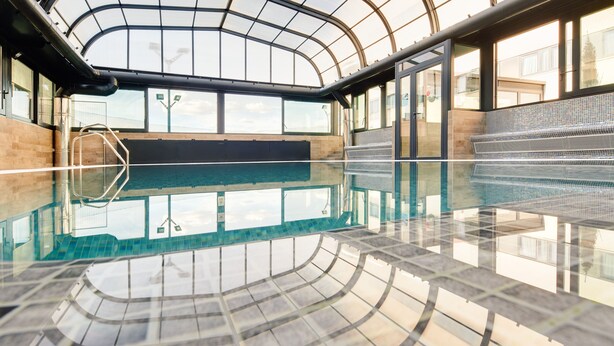 Una piscina interior con techo de cristal, agua cristalina y suelo de baldosas.