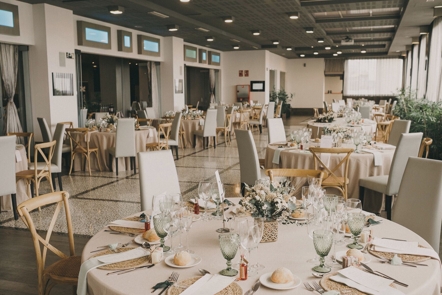 A banquet hall with round tables, chairs, and floral centerpieces.