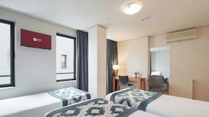 A hotel room with two beds, a desk, a chair, a lamp, a TV, and a window with curtains. - Exe Hotel El Magistral (Oviedo)