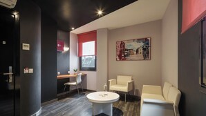 A modern hotel lobby with a round table, two white armchairs, a desk with a computer, and a painting on the wall. - Exe Hotel El Magistral (Oviedo)