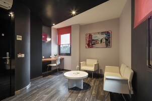 Un moderno vestíbulo de hotel con una mesa redonda, dos sillones blancos, un escritorio con computadora y un cuadro en la pared.