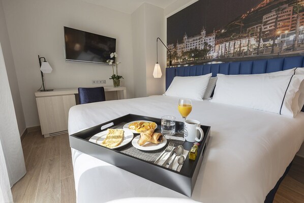 Habitación de hotel con cama, escritorio, silla, bandeja con alimentos para el desayuno y vistas a la ciudad.