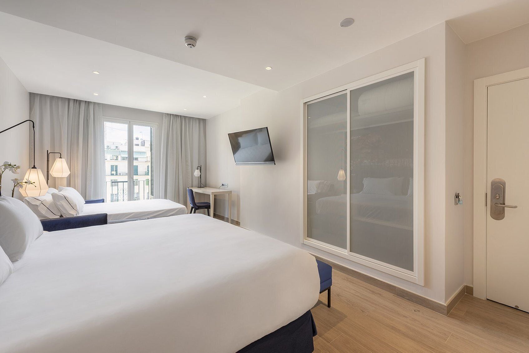 Habitación de hotel con una cama grande, un escritorio, un televisor montado en la pared y un armario con puerta corrediza.
