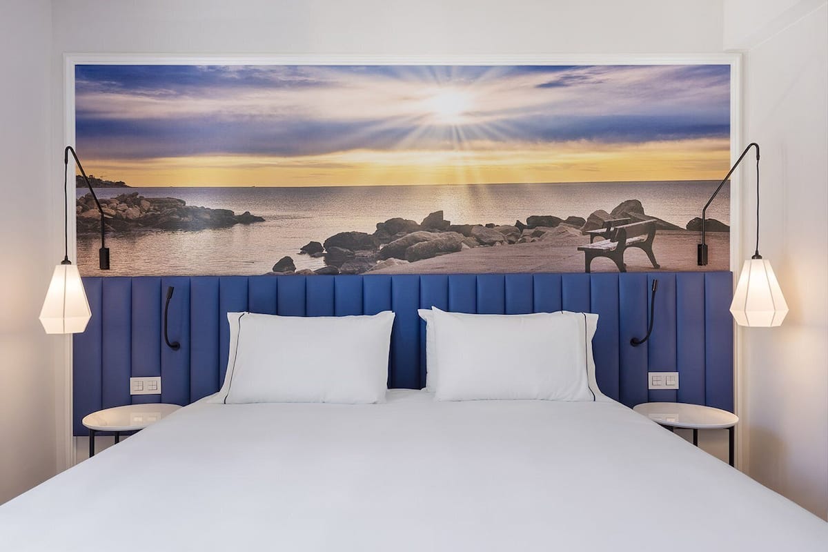 A bedroom with a bed, two bedside tables, a headboard with a sunset view, and pendant lights.