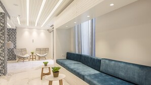 A modern interior with a blue sofa, two wicker chairs, a small round table, and a potted plant. - Eurostars Mediterranea Plaza (Alicante)