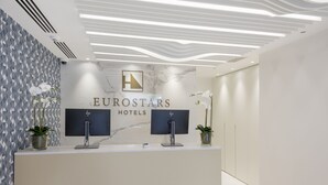 A reception desk at Eurostars Hotels with a marble wall, two monitors, and potted orchids. - Eurostars Mediterranea Plaza (Alicante)