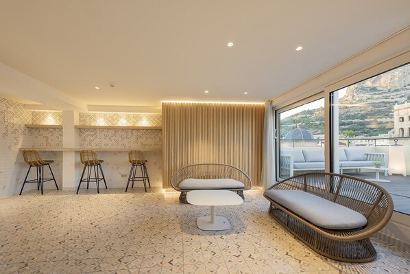 A modern interior with a seating area, bar stools, and a large window offering a view of the outdoors.