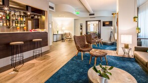 A bar area with stools, a seating area with chairs, a blue carpet, and a TV mounted on the wall. - Best Western Plus CHC Florence (Florence)