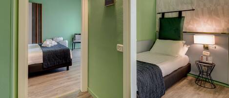 Una habitación de hotel con dos camas, una mesita con una lámpara y una pared verde.
