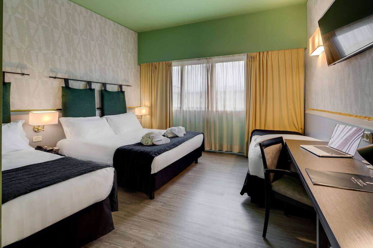 A hotel room with two beds, a desk, a chair, and a TV.