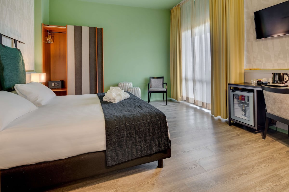 A hotel room with a bed, a desk with a coffee maker, a TV, and a wardrobe.