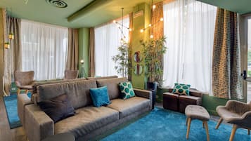 Ein gemütliches Wohnzimmer mit einer Couch, Sesseln, einem kleinen Tisch und einer großen Pflanze.